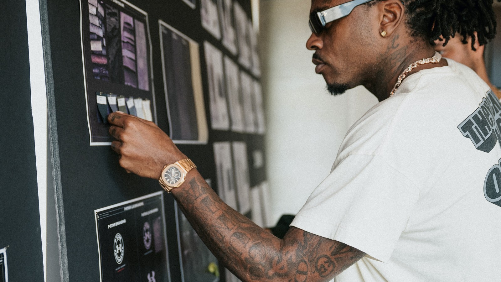 Gunna pinning fabric swatches to a P-Star mood board while wearing a Patek Philippe Nautilus 5712/1R