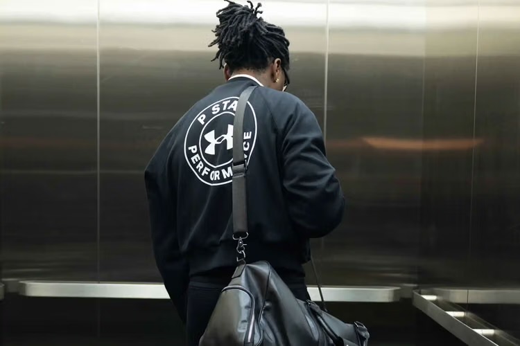 Gunna carrying a duffel bag in an elevator, wearing a P-Star Under Armour jacket